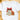 A white short-sleeve crewneck t-shirt laid flat on a light wooden surface, featuring a festive Christmas graphic with a red bow, a gingerbread tree cookie, and a gingerbread man cookie with the text 'Tis the Season'.