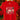 A red short-sleeve crewneck t-shirt hanging on a wooden hanger, featuring a colorful 'Merry CHRIST mas' graphic with Christmas trees and holly. The background shows a blurred Christmas tree with warm string lights.