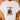 White t-shirt with a skeleton wearing a Santa hat and coffee cup graphic, text 'Look at me being all festive & sh*t' on a wooden background.